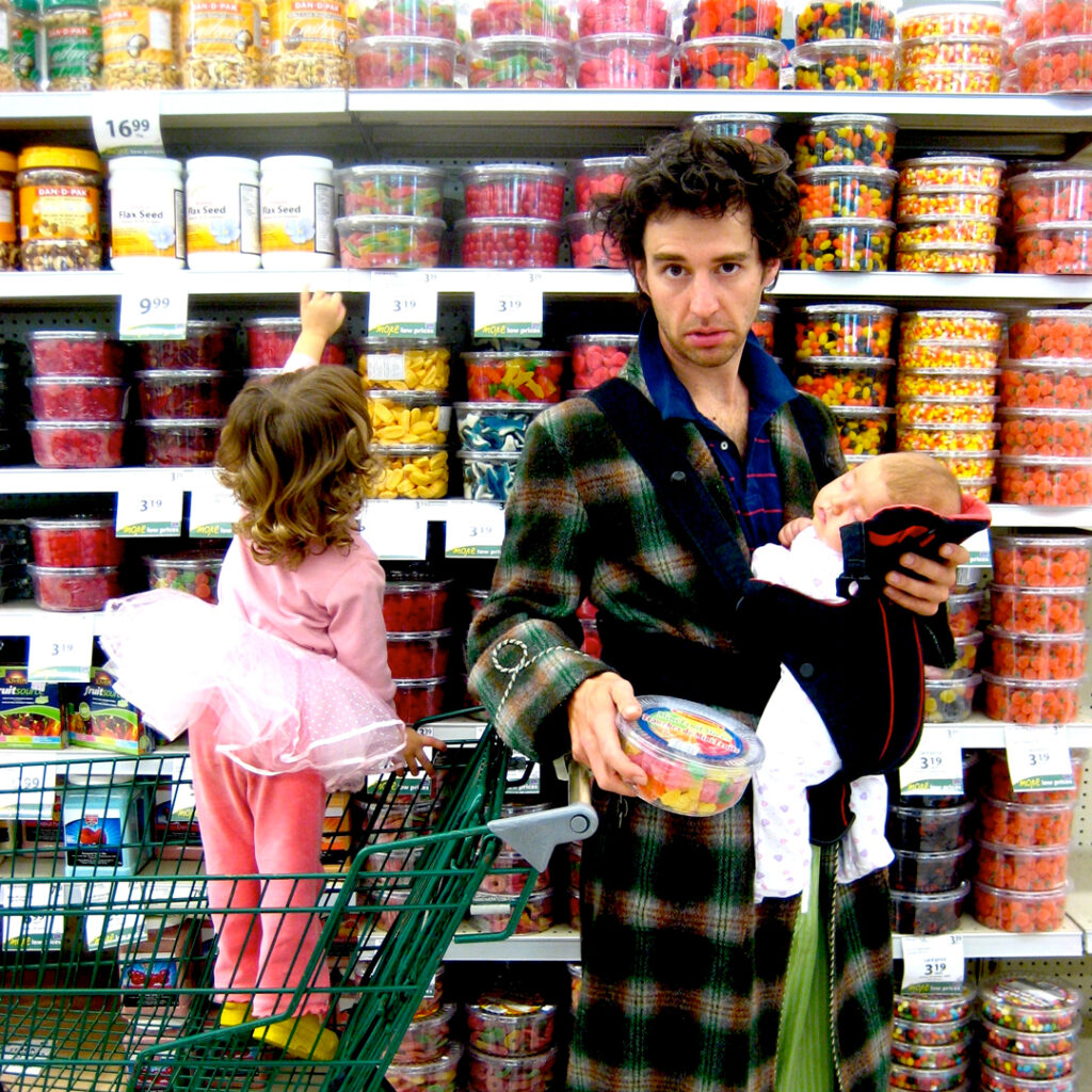 Lucas holding a baby with his other younger child in the shopping cart getting groceries.